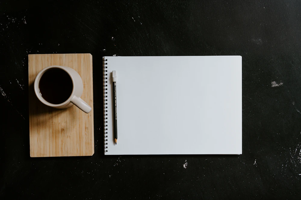 Notizbuch und Bleistift neben einer Kaffeetasse auf einem dunklen Tisch